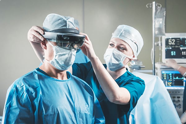 Nurse fitting a headset to doctor's head to engage in augmented reality surgery